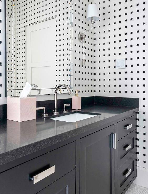 Contemporary black and white bathroom boasts a black washstand accented with a black quartz countertop. A polished nickel faucet kit is fixed beneath a mirror panel framed vanity mirror hung from a wall clad in black and white wallpaper lit by glass sconces.