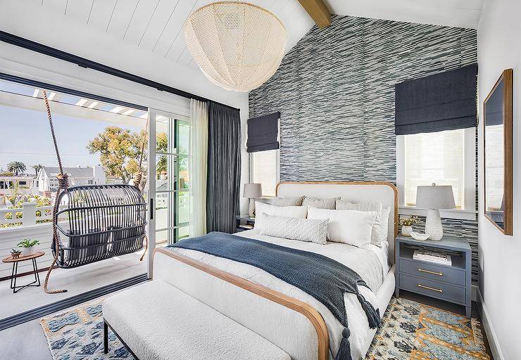 Bedroom features a gray rattan swing on a deck with sliding doors, a white linen bed with wood trim flanked by blue wooden nightstands and white and blue wallpaper.