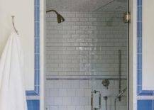 Blue subway tile framed walk in shower with white subway tile inside white towel hanging on wall