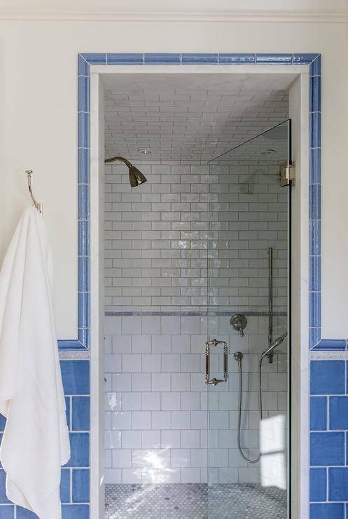 Blue subway tile framed walk in shower with white subway tile inside white towel hanging on wall