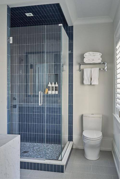 blue vertical subway tile walk in shower with all glass doors toilet with shelf over top and white towels