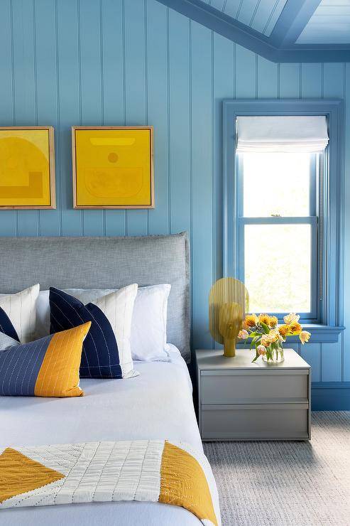 Boy's yellow and blue bedroom features a gray velvet headboard with yellow and blue pillows, vertical blue shiplap trim and a gray modern nightstand.