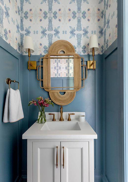 blue wall with wallpaper gold mirror wall sconces in half bathroom with white sink towel rack