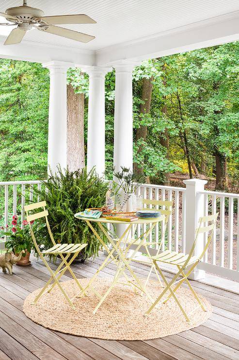 Charming cottage patio features round yellow table and chairs atop a tan round jute rug.