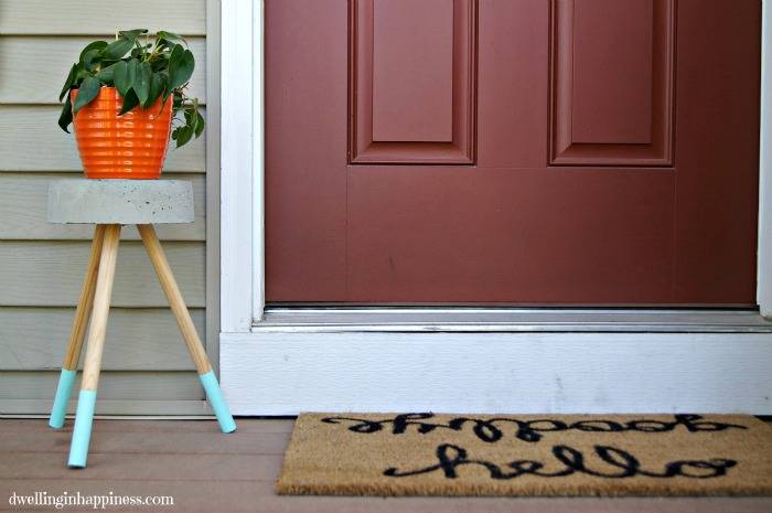 concrete plant stand with wood legs and blue tips orange pot plant by burgundy door