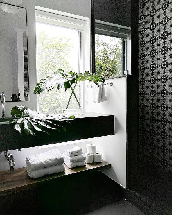 Contemporary bathroom features white black and gray mosaic shower tiles, black floating sink vanity adorned with monstera leaves in vase.