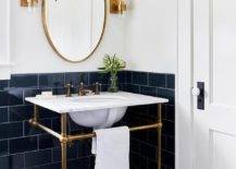 dark navy tile in half bathroom gold oval mirror with candle wall sconces on either side pedestal sink