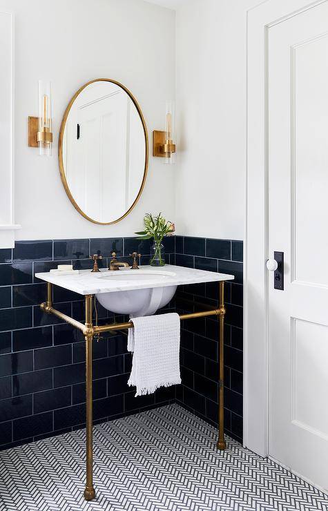 dark navy tile in half bathroom gold oval mirror with candle wall sconces on either side pedestal sink