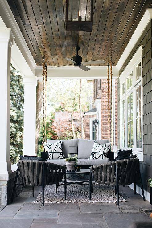 Kelly Wearstler Channels fabric on pillows on a gray outdoor black wooden porch swing designed with a black oval coffee table and black accent chairs on slate pavers.