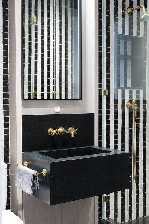 Bathroom features a black marble floating sink vanity with an antique brass cross handle faucet under a tall black box frame mirror.