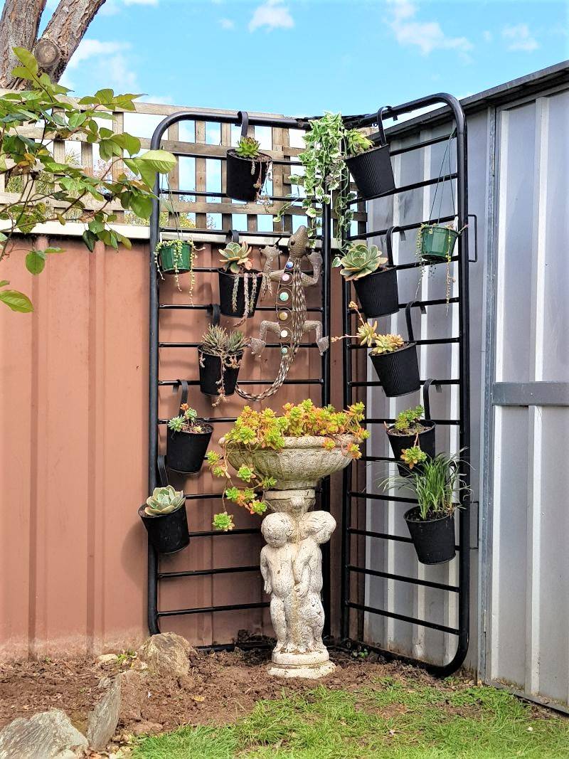 upcycled futon frame to outdoor plant stand with hanging black pots and bird bath beneath