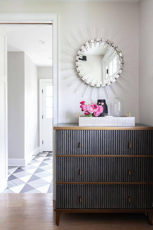 Gray and gold reeded dresser styled with a white tray designed with decor and pink flowers under a lucite sunburst mirror.