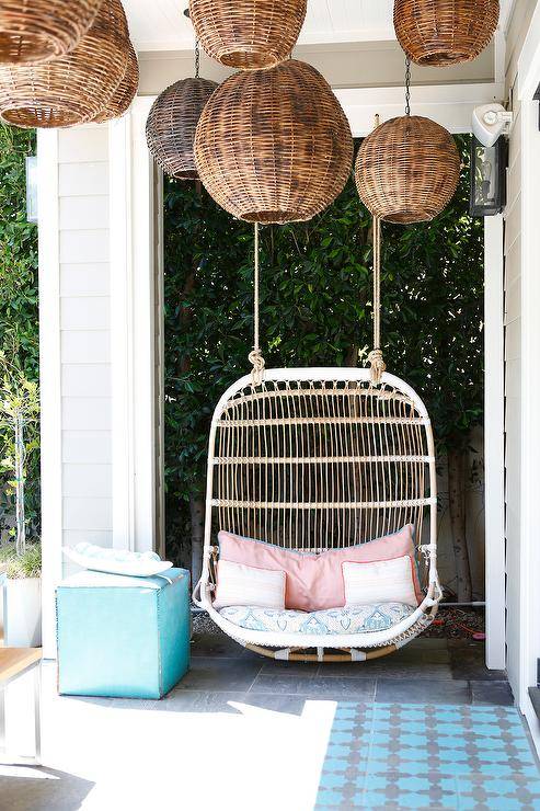 Covered patio features a white rattan swinging chair lit by staggered wicker pendants.