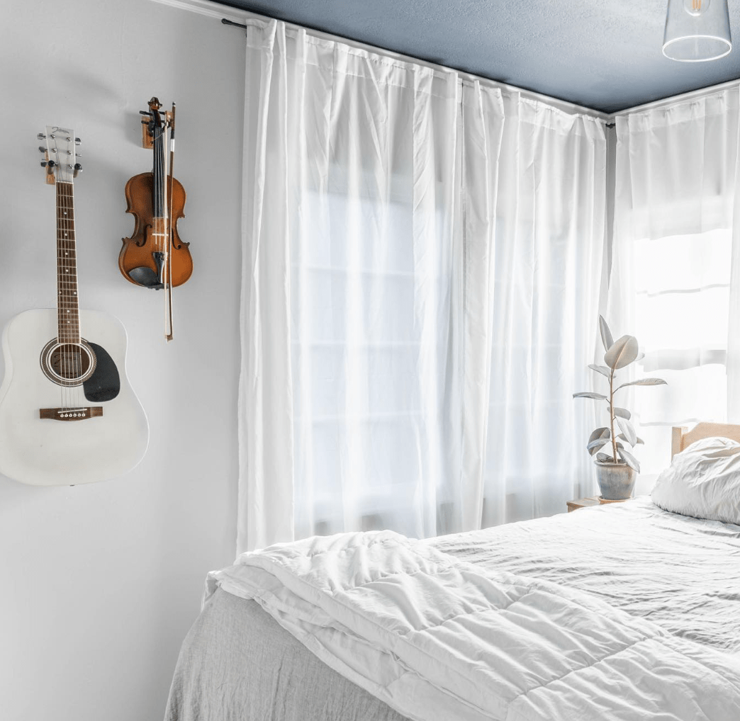 white bedroom with sheer curtains and white bedding with violin and guitar hanging on wall