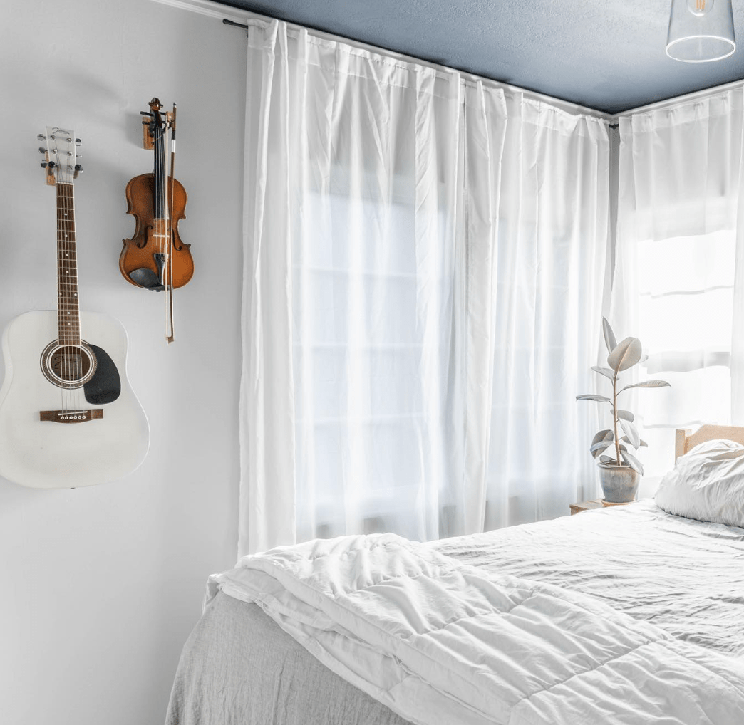 white bedroom with sheer taps and white sheets with violin and guitar hanging on wall