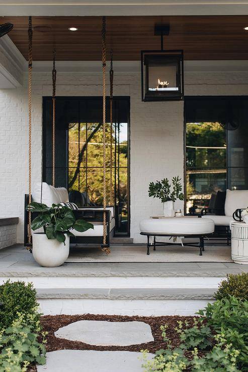 French style white brick home features a small covered patio with swing sofa and a round wrought iron ottoman.