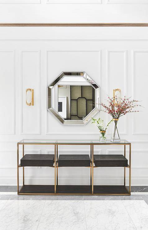 Adding an octagon beaded mirror on a millwork foyer wall accents the overall appeal as you walk into an entryway. A glass and brass console table styles the space atop gray and white marble floor tiles for a classic finish.