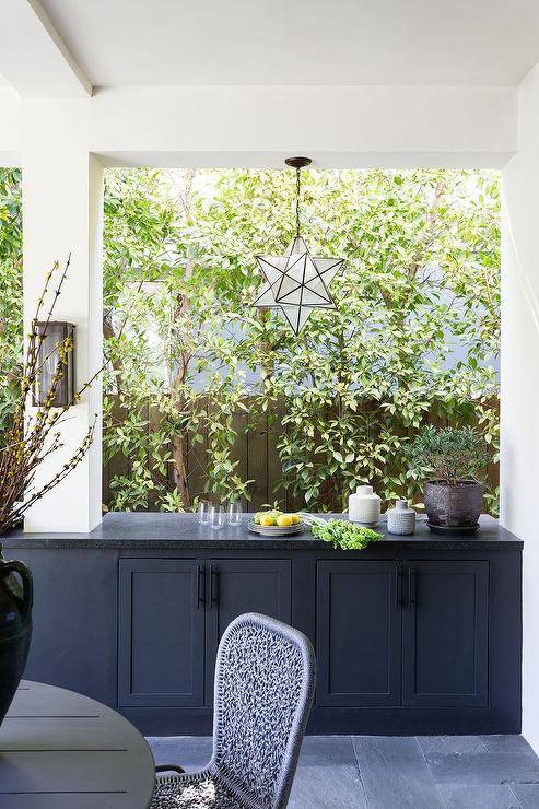 Transitional covered patio features outdoor black buffet cabinet topped with black granite illuminated by a moravian star pendant.