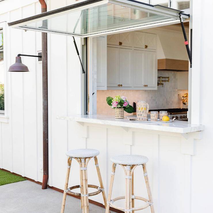 Backelss French bistro stools sit at a pass through patio bar fitted with a garage style window.