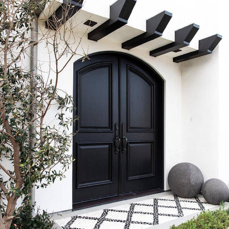 Mediterranean style home with white stucco features black double front doors with stylish black and white porch tiles and gray cement boulder accents. Black beams accent the white stucco completing an updated and trendy porch design.