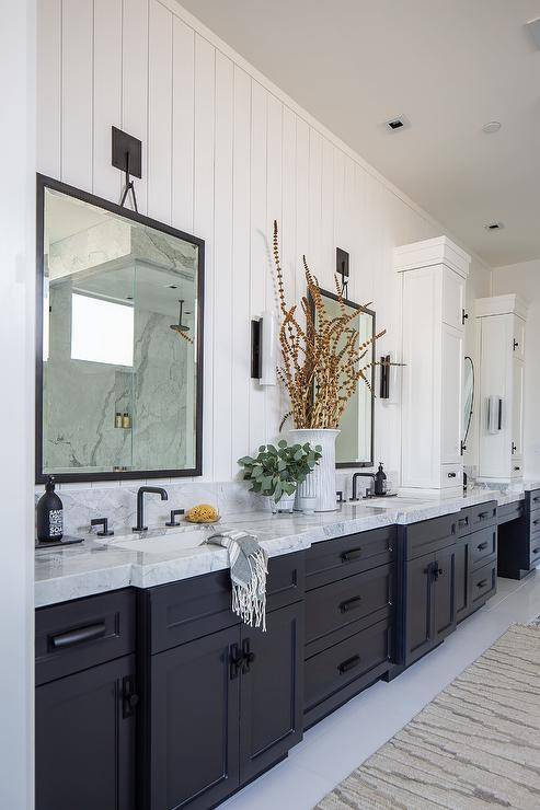 Black and white master bathroom features black vanity mirrors hung from a vertical shiplap wall over a black dual washstand donning matte black hardware and a white and gray marble countertop finished with matte black faucets.