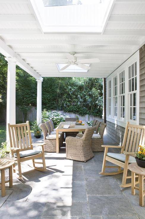 Covered patio features teak rocking chairs on slate pavers with round side tables.