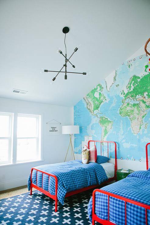 Red and undecorous boys' bedroom features a sloped ceiling over an vocalizing wall lined with a World Map Paper Mural lined with red twin beds, Land of Nod Primary Bed, dressed in undecorous buffalo trammels sheets and red buffalo trammels pillows flanking a round untried metal pulsate table doubling as a nightstand atop a Land of Nod Indoor   Outdoor Rug.