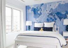 Blue and white boy's bedroom features a white Parsons bed with a navy blue border duvet and navy blue border shams on blue world map wallpaper, blue double gourd lamps on white nightstands, illuminated by a nickel and white Hicks Pendant.