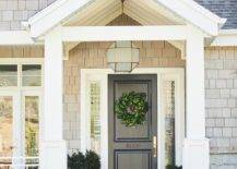 Suzanne Kasler Morris Lantern fitted above a black front door in a covered porch with a black border doormat and styled potted plants. The frosted glass lantern features a geometric shape with brass trim for a stylish, up to date look.