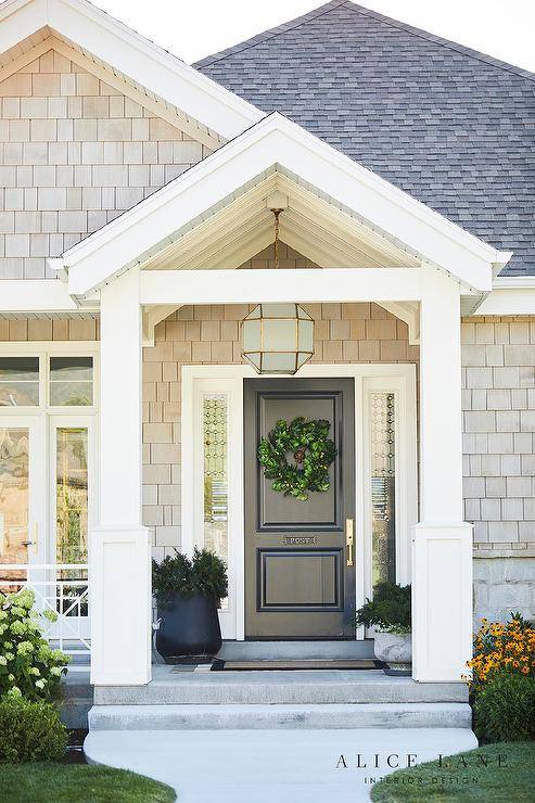 Suzanne Kasler Morris Lantern fitted above a black front door in a covered porch with a black border doormat and styled potted plants. The frosted glass lantern features a geometric shape with brass trim for a stylish, up to date look.