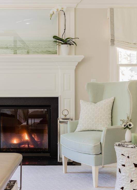 Pastel color tones in a master bedroom deliver a relaxed and inviting appeal showcased on a mint green accent chair near a fireplace mantel paired with a white cloud stool accent table.