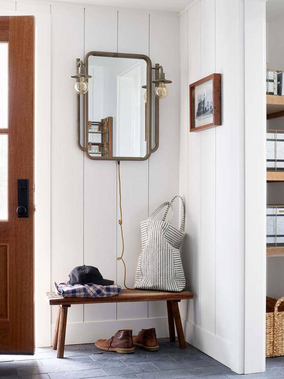 mirror in entryway with farmhouse industrial style sconces wooden bench