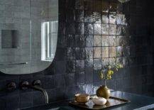 Modern black bathroom features black glazed grid tiles, an oblong vanity mirror over a black wooden floating sink vanity with a black leathered countertop and a matte black wall mount faucet.