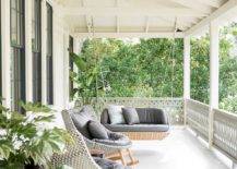 Covered porch features white painted floors, a wicker hanging sofa and gray wicker wingback rockers.