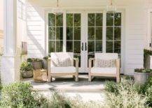 styled covered porch boasts hand blown glass lanterns hung over Restoration Hardware Aegean Teak Chairs placed beside gray planters and in front of sliding glass doors framed by white siding