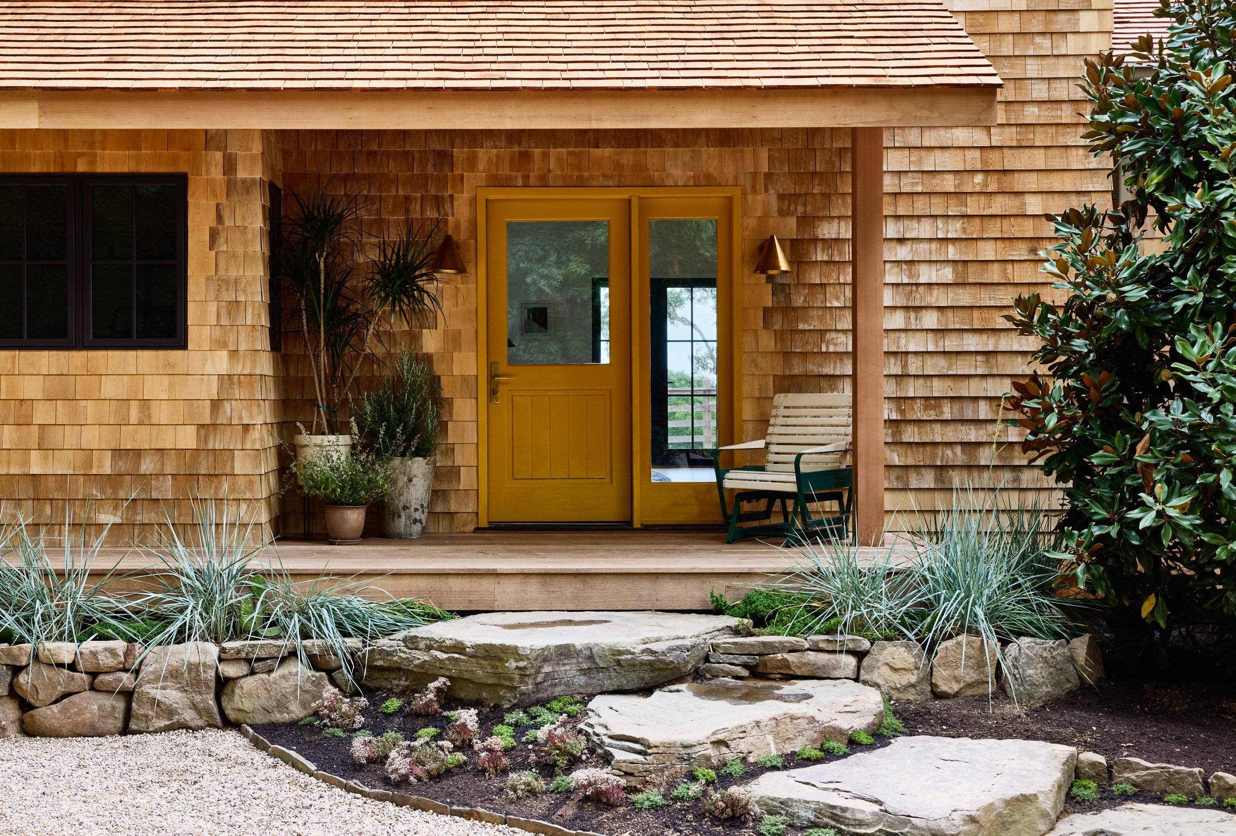 mustard front door on cedar shake sided house with rock path