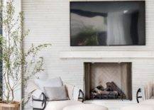 Spacious covered patio features white fireplace wall split face tiles under a mounted TV and an off white accent chair with off white ottoman atop a tan rug.