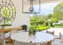 Stunning covered patio is lit by an iron lantern hung over a round white table surrounded by folding chairs, while a round mirror hangs above a wooden console table.