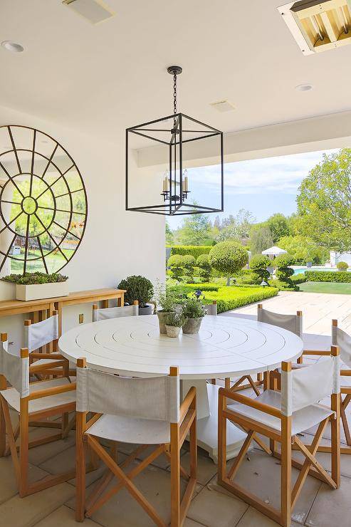 Stunning covered patio is lit by an iron lantern hung over a round white table surrounded by folding chairs, while a round mirror hangs above a wooden console table.