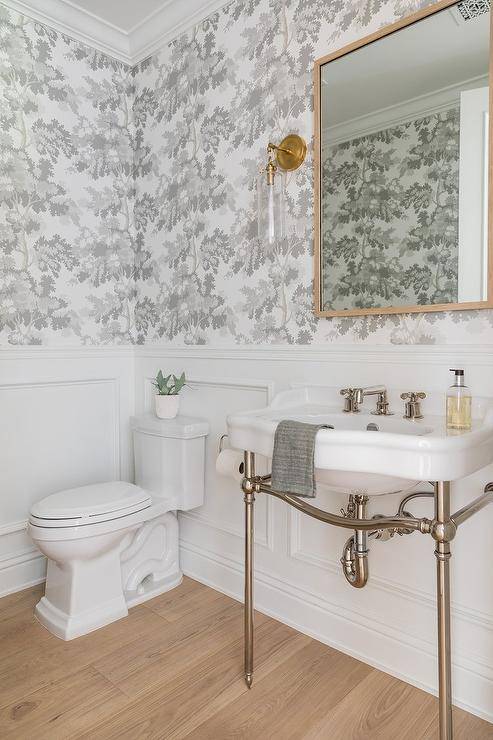 half bathroom with floral grey wallpaper polished nickel pedestal sink toilet gold square frame mirror wall sconce