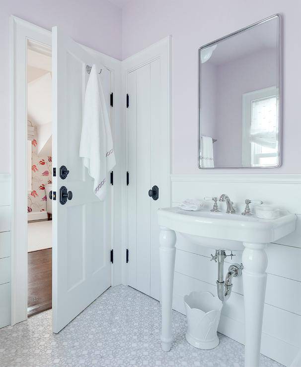 white pedestal sink in lavender color bathroom with door half open black door knobs silver polished mirror