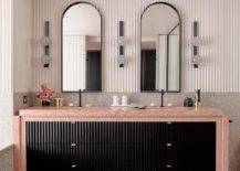 Modern bathroom features a black bath vanity with pink marble countertop under black arched vanity mirrors flanked by bulb sconces on gray mosaic backsplash tiles.