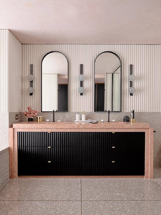 Modern bathroom features a black bath vanity with pink marble countertop under black arched vanity mirrors flanked by bulb sconces on gray mosaic backsplash tiles.