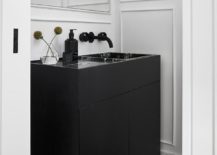 Chic black and white powder room features a black sink vanity fitted with a black marble sink matched with a matte black wall mount faucet fixed to a wainscot wall under a frameless vanity mirror.