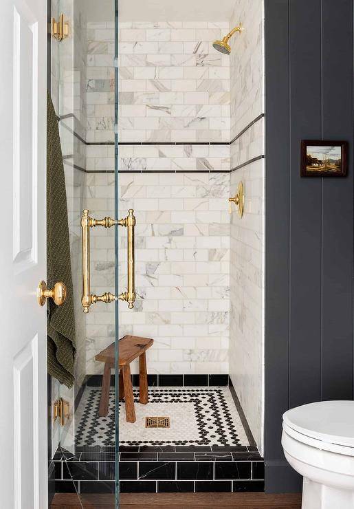 small walk in shower with marble subway tiles glass door with gold hardware black floor tile