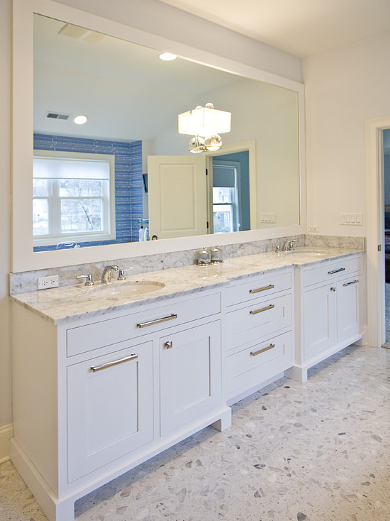 White double vanity with white marble countertop. Terrazzo flooring, double wide framed mirror