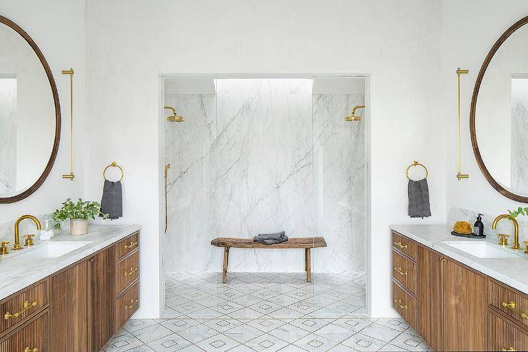 symmetrical bathroom matching vanities wood black round frame mirrors decorative floor tiles gold faucets bench in shower glass doors
