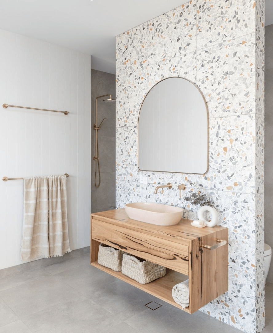 terrazzo accent wall in bathroom arch framed gold mirror wood floating vanity with pink sink