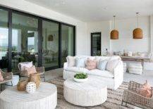 A white slipcovered sofa accented with blue and pink pillows sits on a gray Moroccan wedding blanket rug facing two round faux bois coffee tables located under a covered patio. The coffee tables are flanked by facing wicker accent chairs.