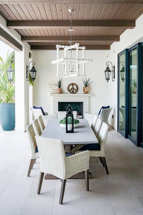 Light gray wicker dining chairs designed around a wood and concrete trestle dining table in an outdoor covered patio.